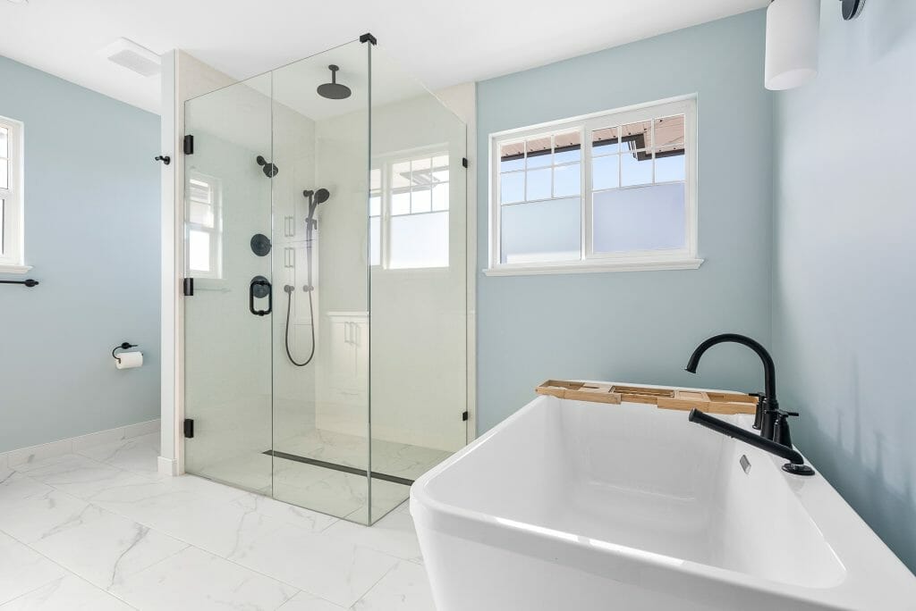 Panoramic view of a renovated bathroom with a large soaker tub, a walk-in glass shower, and white marble flooring.