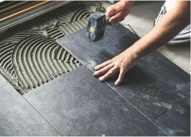 A person installing grey tile flooring.