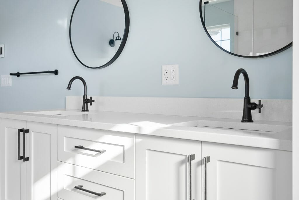 A modern bathroom renovation with a double sink, white cabinets and dark metal fixtures.