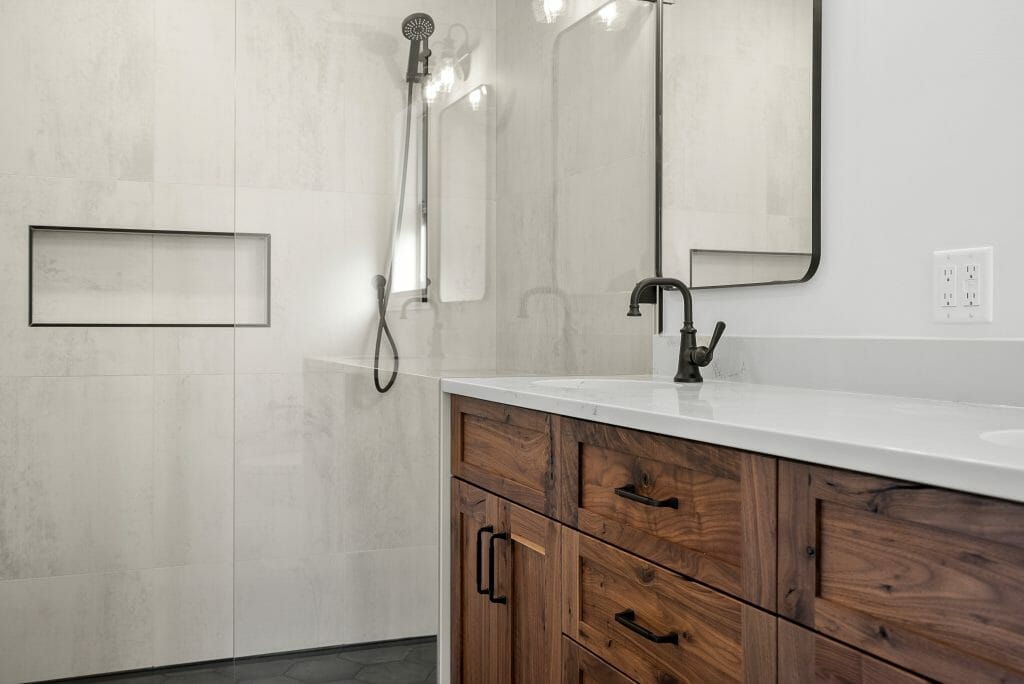 A refinished bathroom with wood grain cabinets and modern dark brass bathroom fixtures.