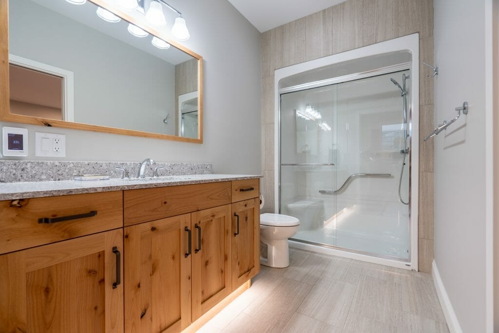 A large refinished bathroom with natural wood cabinets and a large shower with glass doors.