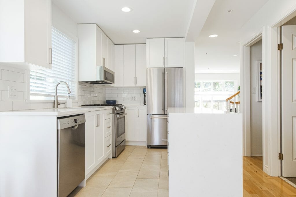 A white refinished modern kitchen with tile flooring and stainless steel appliances.