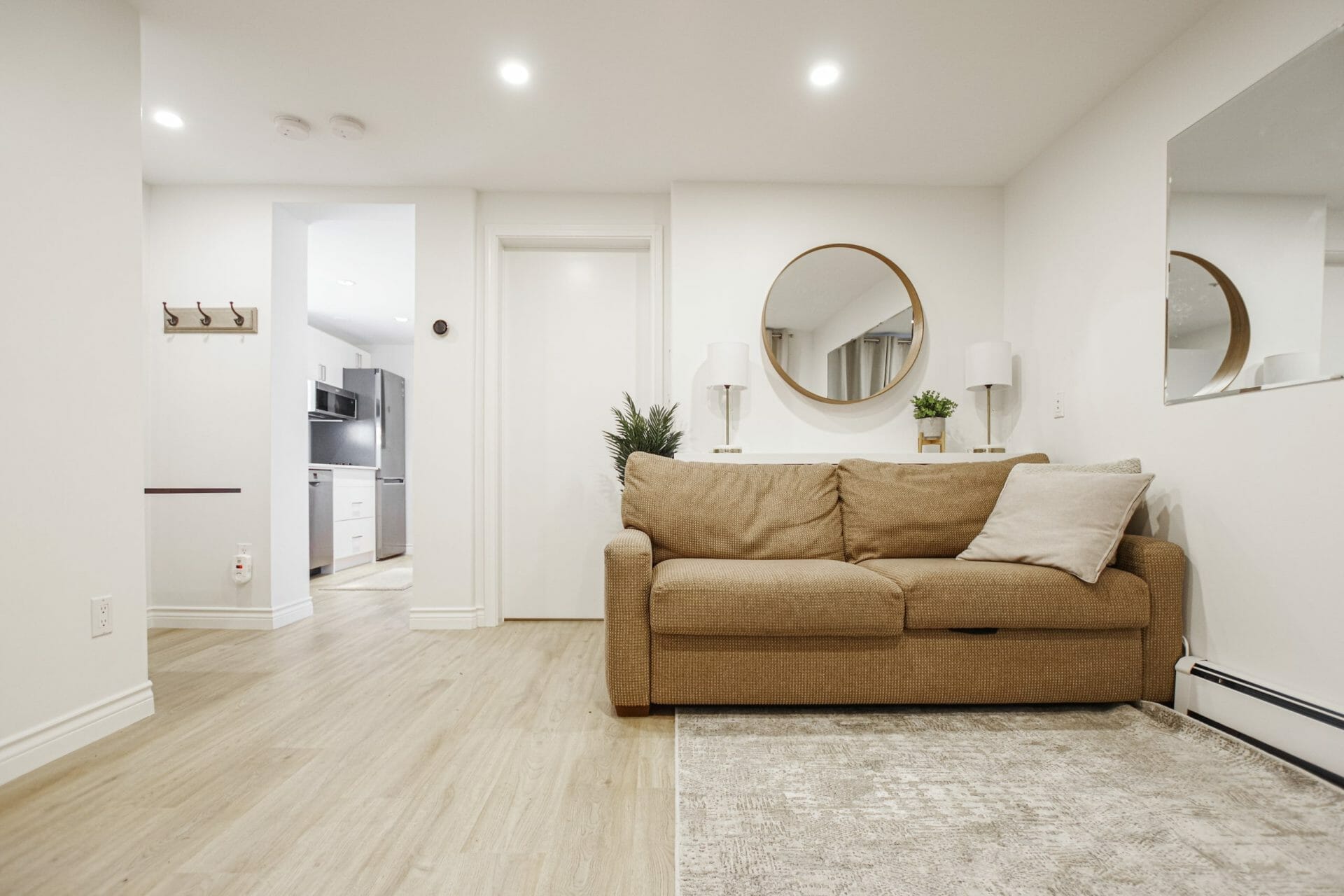 A finished basement suite with a baseboard heater, brown couch, and a small kitchen in the background.